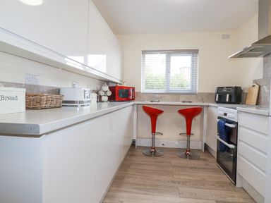 A kitchen with white cabinets two red bar stools and appliances at Falcon House in Tintagel