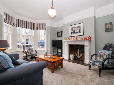 A living room with striped armchairs a wooden coffee table a fireplace and a television at Elkhorn in Southwold