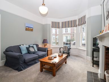 A living room with a blue sofa wooden coffee table armchair and bay windows at Elkhorn in Southwold