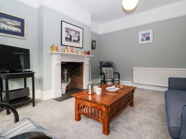 A living room with a wooden coffee table cups and plates an armchair a television on a stand and a fireplace at Elkhorn in Southwold