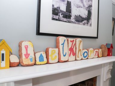 Painted stones arranged on a white mantelpiece with small decorative houses and a framed black and white photo above at Elkhorn in Southwold