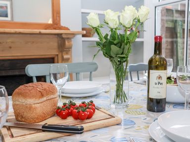 A dining table with bread cherry tomatoes a knife a bottle of wine white roses and empty plates at Elkhorn in Southwold
