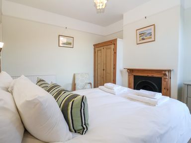 A bedroom with a bed, pillows, folded towels, a wooden wardrobe, a fireplace, and two framed pictures on the walls at Elkhorn in Southwold