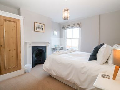 A bedroom with a double bed bedside table with lamp a window fireplace and wooden door at Elkhorn in Southwold