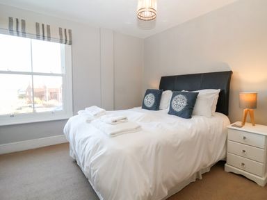 A bedroom with a bed with white linens and blue decorative pillows next to a white nightstand with a lamp at Elkhorn in Southwold