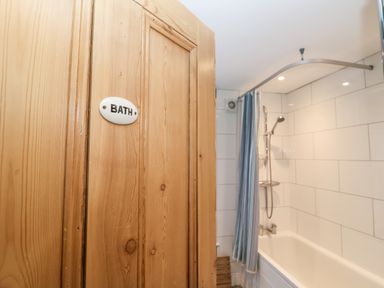 A wooden door with a bath sign opening to a bathroom with a bathtub shower and a blue and white striped shower curtain at Elkhorn in Southwold