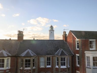 Rooftops of brick houses with chimneys and a lighthouse in the background in Southwold