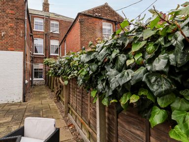 A paved narrow backyard area with wooden fencing covered in green ivy next to a red brick building at Elkhorn in Southwold