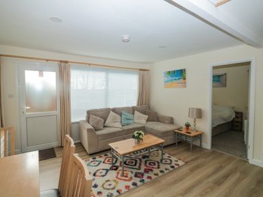 A living room with a sofa pillows coffee table and a dining table with chairs at The Bolthole in Dartmouth