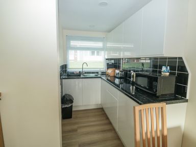 A kitchen with black countertops white cabinets a sink a microwave toaster and a wooden chair at The Bolthole in Dartmouth