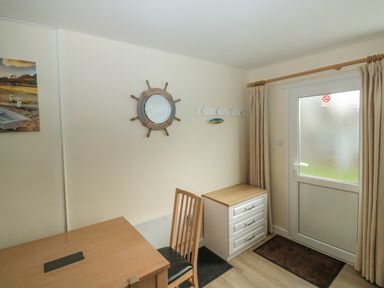 A room with a wooden desk and chair a three-drawer cabinet a wall clock shaped like a ship wheel a coat rack and a door with curtains at The Bolthole in Dartmouth