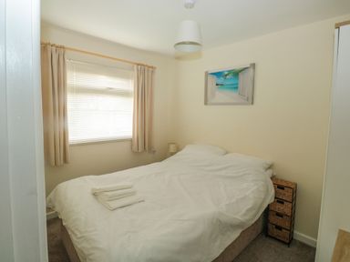 A bedroom with a double bed white bedding folded towels on bed small lamp window with blinds and curtains at The Bolthole in Dartmouth