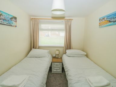 A bedroom with two single beds with white bedding and a nightstand with a lamp in between at The Bolthole in Dartmouth