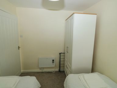 A small bedroom with two single beds a white wardrobe a clothes drying rack and a door at The Bolthole in Dartmouth