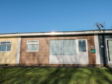 A single-story building with brown wood paneling white door and windows and a green mailbox on a grassy area at The Bolthole in Dartmouth