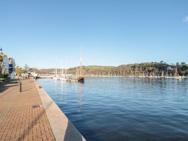 A marina with boats docked near a paved walkway and a wooded hill in the background at The Bolthole in Dartmouth