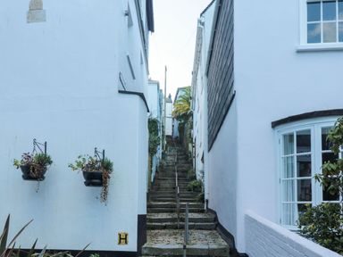 A narrow stone staircase between white buildings with hanging plants and a handrail at The Bolthole in Dartmouth