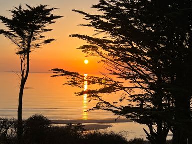 Sun setting over calm water with trees in the foreground at Sibrwd Y Mor in Harlech