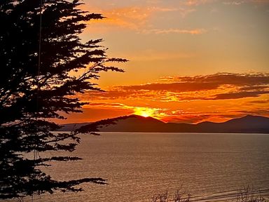A sunset over a body of water with silhouetted tree and hills in the background at Sibrwd Y Mor in Harlech