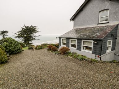 A gravel driveway next to a house with windows overlooking trees and the sea at Sibrwd Y Mor in Harlech