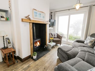 A living room with a fireplace armchair sofa and sliding glass doors at Sibrwd Y Mor in Harlech