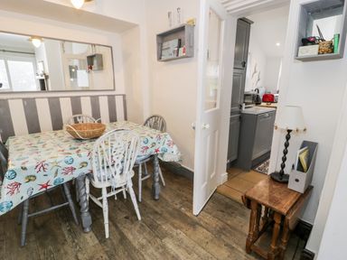 A dining area with a table covered in a seashell tablecloth and chairs next to a kitchen with grey cabinets at Sibrwd Y Mor in Harlech