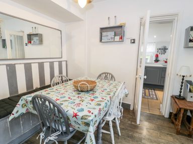 A dining room with a table covered with a seashell patterned cloth and chairs around it at Sibrwd Y Mor in Harlech