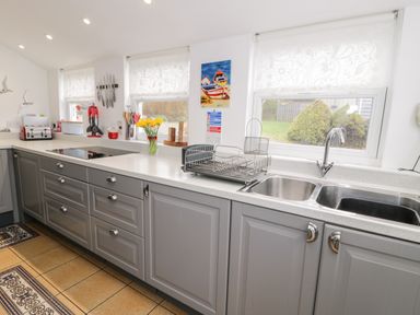 A kitchen with grey cabinets a double sink a dish rack and yellow flowers in a vase at Sibrwd Y Mor in Harlech