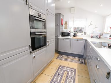 A kitchen with grey cabinets built in oven microwave kettle toaster and decorative tiled floor at Sibrwd Y Mor in Harlech