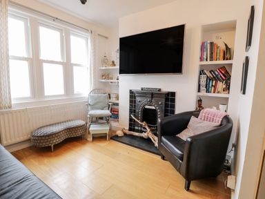 A living room with a black armchair pillows television above fireplace bookshelf and window at Sibrwd Y Mor in Harlech