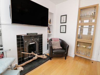 A corner of a living room with a black leather chair next to a fireplace and a glass cabinet containing glassware at Sibrwd Y Mor in Harlech