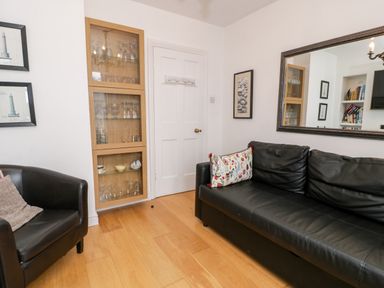 A sitting area with a black leather sofa and chair a glass cabinet a white door and wall art at Sibrwd Y Mor in Harlech