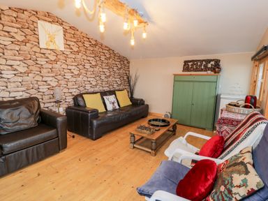 A living room with leather sofas wooden floor a green cabinet and various cushions at Sibrwd Y Mor in Harlech