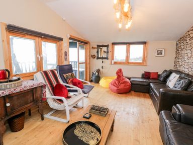 A living room with wooden floors leather sofa bean bags and armchairs at Sibrwd Y Mor in Harlech