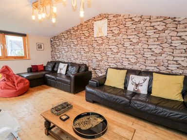 A living room with two black leather sofas a wooden coffee table and a red bean bag at Sibrwd Y Mor in Harlech