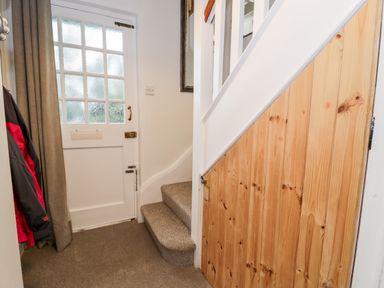 An entrance hallway with a white door and stairs next to a wooden under stair storage at Sibrwd Y Mor in Harlech