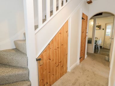 A hallway with carpeted stairs and wooden doors leading to under stairs storage and another room at Sibrwd Y Mor in Harlech
