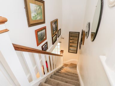 A carpeted staircase with framed pictures and mirrors on the walls at Sibrwd Y Mor in Harlech
