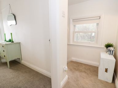 A small hallway with a green chest of drawers and mirror on one side and a white cabinet with a plant and decorative items near a window at Sibrwd Y Mor in Harlech