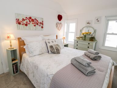 A bedroom with a bed decorated with pillows and towels beside a dresser with flowers and two windows at Sibrwd Y Mor in Harlech