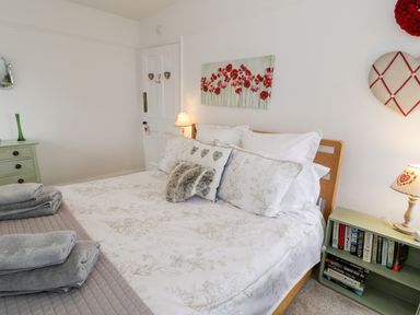 A bedroom with a bed with pillows and folded towels beside a small bookcase with a lamp and books at Sibrwd Y Mor in Harlech