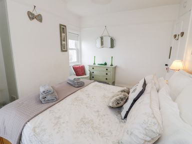 A bedroom with a bed a dresser a chair with a cushion and a wall mirror at Sibrwd Y Mor in Harlech