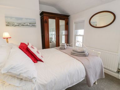 A bedroom with a bed with white and red pillows a wooden wardrobe towels on the bed and an oval mirror on the wall at Sibrwd Y Mor in Harlech