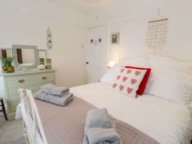 A bedroom with a large bed with pillows and folded towels a dresser with mirrors and a plant a door and wall decorations at Sibrwd Y Mor in Harlech