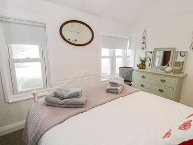 A bedroom with a bed with folded towels a green dresser with a mirror and windows with blinds at Sibrwd Y Mor in Harlech