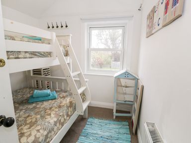 A small bedroom with bunk beds a blue striped rug and a window at Sibrwd Y Mor in Harlech