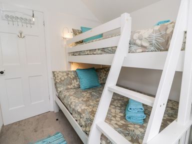 A small bedroom with a white bunk bed and floral bedding at Sibrwd Y Mor in Harlech