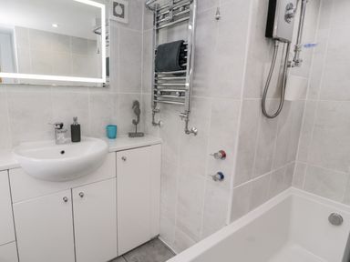 A bathroom with a sink and cabinet next to a bathtub with a shower and towel rail at Sibrwd Y Mor in Harlech