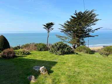 A grassy garden with bushes and trees overlooking the ocean with a sandy beach at Sibrwd Y Mor in Harlech