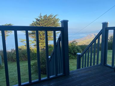 A view from a wooden deck with railings overlooking trees grass and a coastline at Sibrwd Y Mor in Harlech